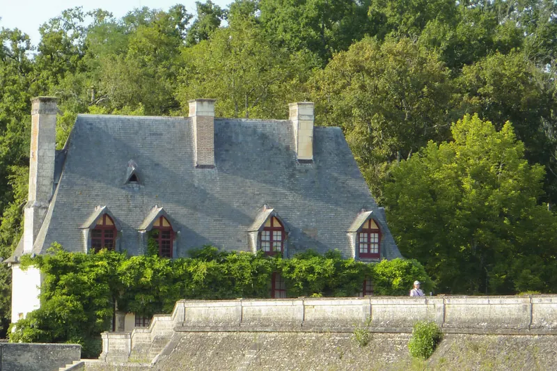 Maison au toit d’ardoise couverte de glycine, au bord de l’eau, deux barques amarrées contre le mur de pierre.