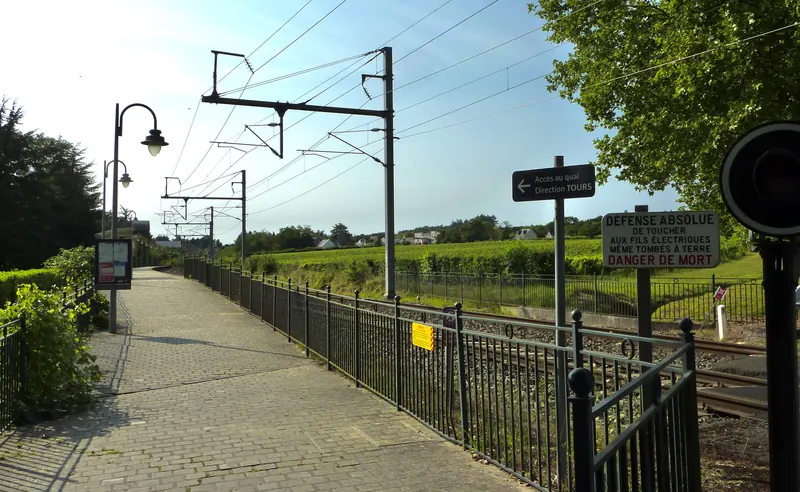 Quai de la gare de Chenonceaux, panneau « Accès au quai, direction Tours », rails et vignes en arrière-plan.